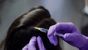 A beautician conducts mesotherapy for hair in gloves with using a professional medical product in the cosmetology center. Close-up.
