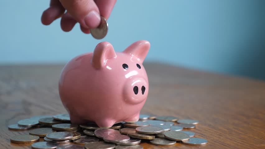 Piggy bank business standing on a pile of coins concept. A hand is putting a coin in a piggy bank on lifestyle a yellow background. saving money is an investment for the future. Banking investment and | Shutterstock HD Video #1025625953