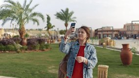 Woman in red shirt and jeans jacket makes mobile photos of the sights, sightseeing on vacation, mobile photography