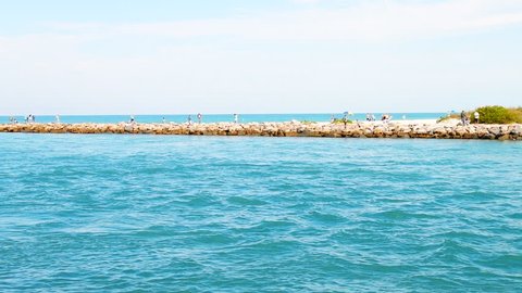 Venice, Florida with people on fishing boat swimming by rocky pier in slow motion in Florida retirement beach city, town or village in gulf of Mexico