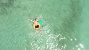 Drone point of view of young man relaxing on inflatable pineapple floating on sea. People travel beach holidays concept. Aerial view directly above of male enjoying freedom on tropical Islan vacations