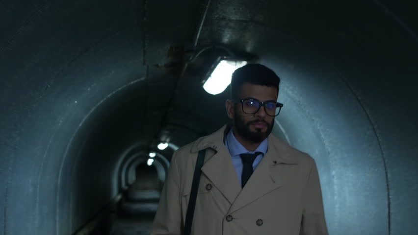 Up section shot of young Middle Eastern businessman walking through tunnel in the evening