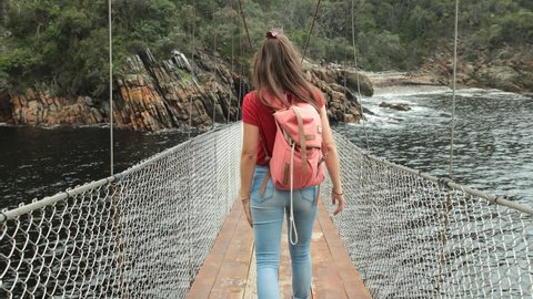 Girl walking over suspension bridge in a beautiful nature park. Shot on a Glidecam in 4k at 60fps so it can be slowed down if desired.