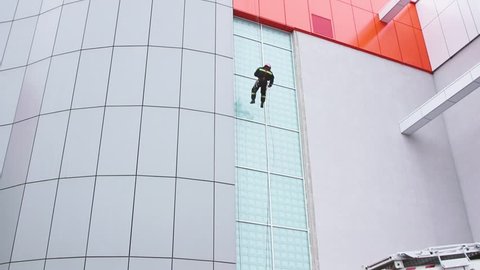 Fireman descending hanging on a glassy building facade on a rope