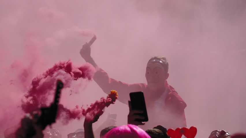 Casa De Papel costume carnival parade participant holds flare. Person with Salvador Dali hoodie red jumpsuit costume marching holding a lit flare in dense smoke in Xanthi, Greece.