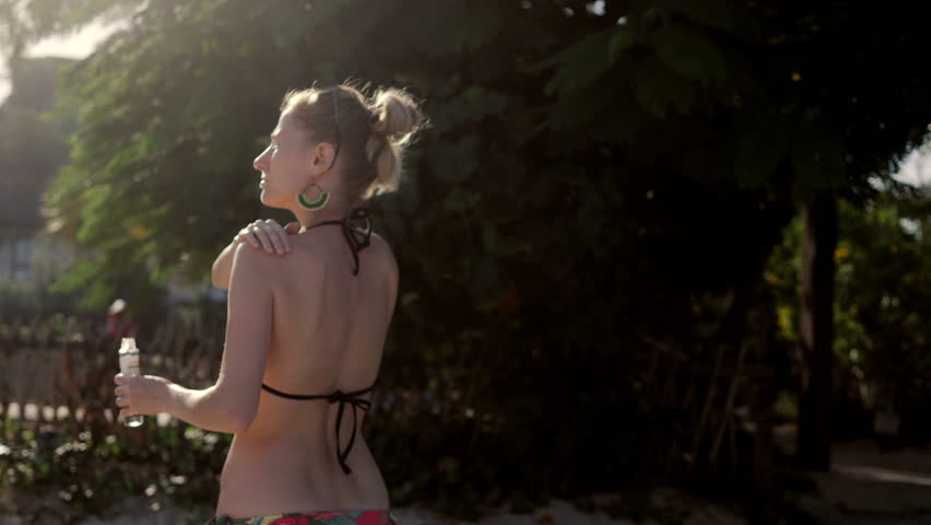 Woman body oils. Young woman in bikini creams her body. Green tree background