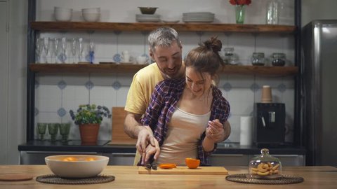 Portrait of lovely couple having fun in kitchen, laughing and eating orange. Cute spouses making dinner together. Love and relationships concept