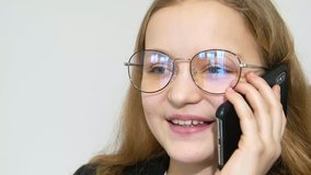 Talk about business. Cheerful little girl in official clothes talking on a mobile phone, sitting at the computer on a white background, 4k video