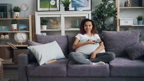Zoom-in of pretty African American student watching funny comedy on TV and laughing sitting on sofa and holding remote control. Television and emotions concept.