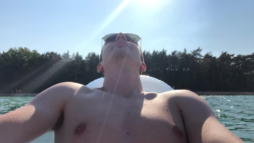 Young man relax on inflatable deck chair on lake during sunny day
