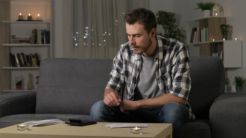 Confused man reading receipts sitting on a couch in the night at home