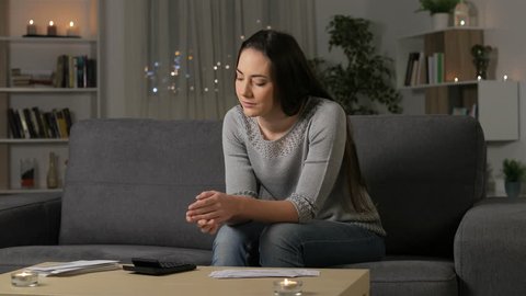 Confused woman reading bank receipts in the night sitting on a couch at home