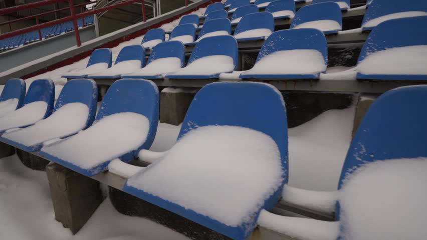 Rows of blue plastic seats on stadium tribune covered with snow in winter