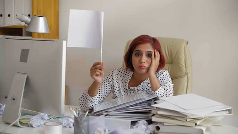 Lockdown of Indian businesswoman sitting at desktop with white flag in her hand then putting head on her arms lying on document folders