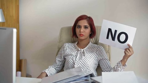 Lockdown of young Indian businesswoman sitting on chair in her office with nameplate in her hand, looking at camera and saying no to offer