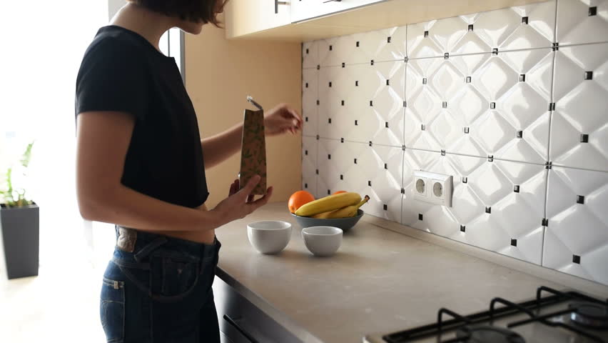 Beautiful young couple is talking and smiling while cooking healthy food in kitchen at home. The wife makes tea and her husband embraces her.
