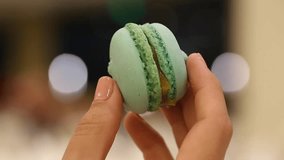 Closeup view of green tasty macaroon in hands of woman. Real time full hd video footage.