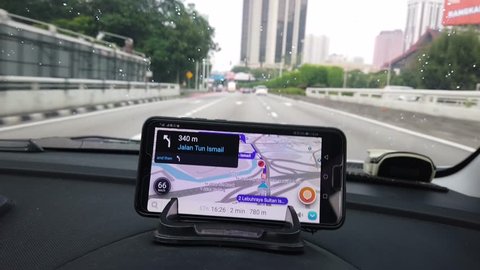 MALAYSIA, Kuala Lumpur, March 10, 2019: Waze application on the smartphone shows the road direction on the car dashboard when the rains are visible in the windscreen while the wiper works.