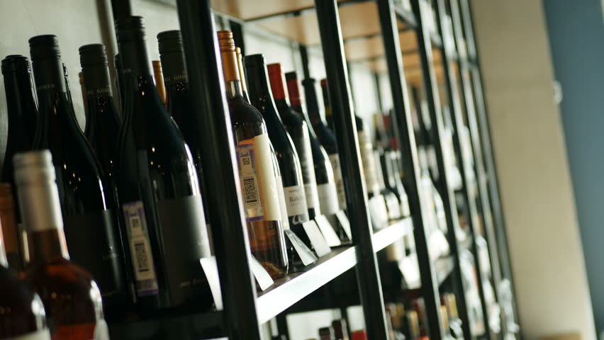 Young man taking a bottle of wine from the counter at the supermarket and reading the ingredients. View from the side.