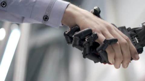 Future is now. Male hand of young student scientist inventor shakes robotic arm. Hand of a man shaking hands with robot. Robotic and human hands join in a handshake.