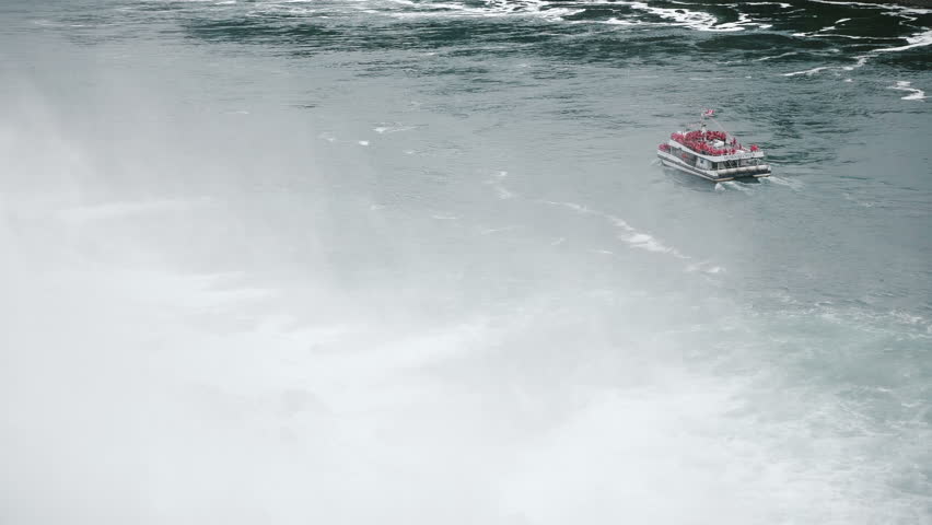 Amazing high angle view of waterfall spray and tourist boat full of people coming close to epic Niagara fall slow motion