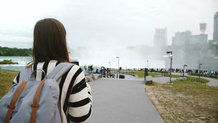 Camera follows thoughtful local woman walking towards crowded observation deck at mighty Niagara waterfall slow motion.