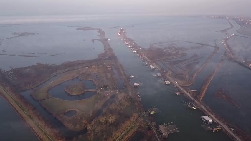 Aerial view at dawn of the Comacchio lagoon in the Po river Delta park. You can see fishing huts and small low clouds