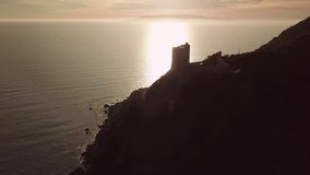 Aerial romantic view of a sunset over the sea with an ancient tower in backlight
