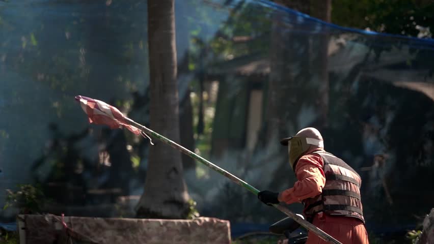Man in Orange Suit with Gun and Protective Mask Running with Victory Flag Playing Paintball Game on Paintball Field with Tires and Wooden Shelters in Forest. Extreme Team Sport