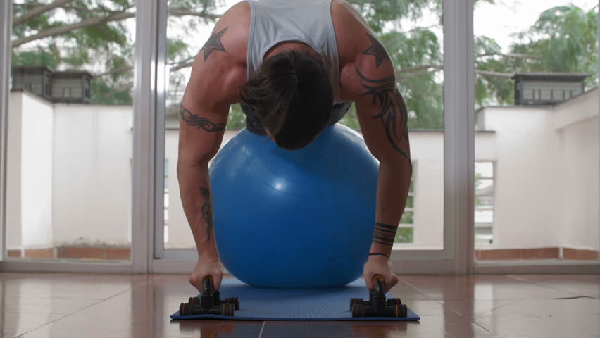 Wide shot of Caucasian sporty man pumping muscles with fit ball and push up bars