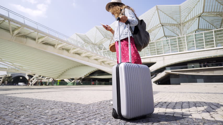 Back view of lady in hat with knapsack and baggage going to Oriente railway station in Lisbon