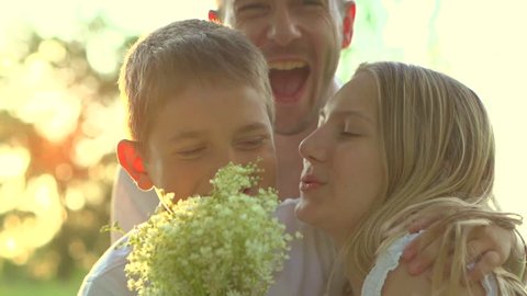 Happy family. Father, Mother and their little son with bouquet of flowers outdoors. Mom, dad and kid kissing and hugging. Mother's day gift. Slow motion, high speed camera shot. Full HD 1080p