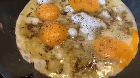 Video of cooking of fried eggs from several eggs with onions and black pepper, liquid egg white, a teflon frying pan, bubbles, steam, omelet