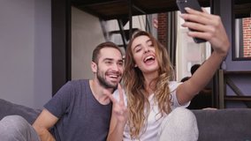 Cheerful lovely couple making selfie on smartphone while sitting on sofa