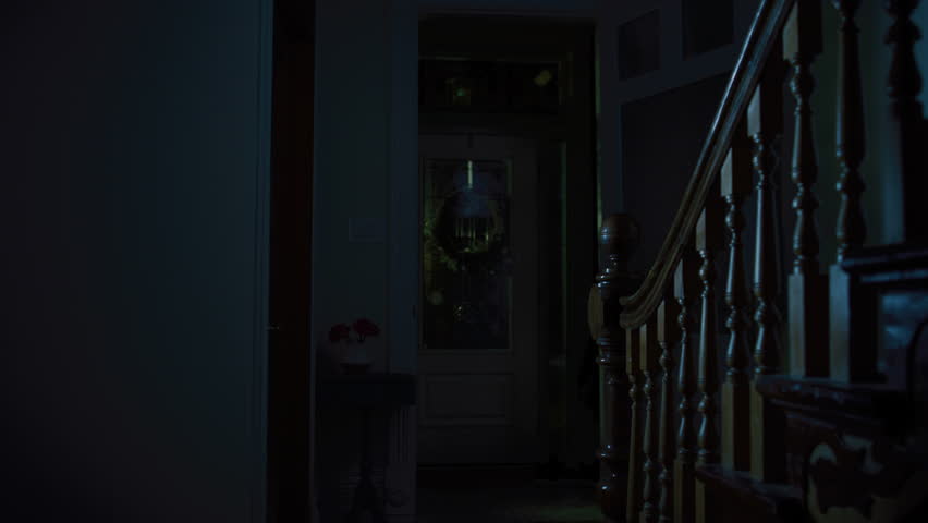 A woman with a flashlight walks downstairs in a dark house at nighttime.  Royalty-Free Stock Footage #1025731580