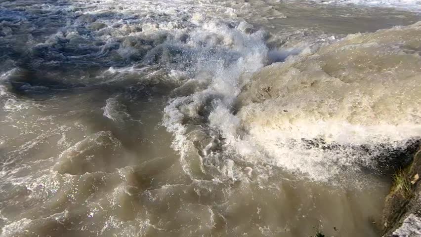 Dirty flood waters gushing over a man made wall.