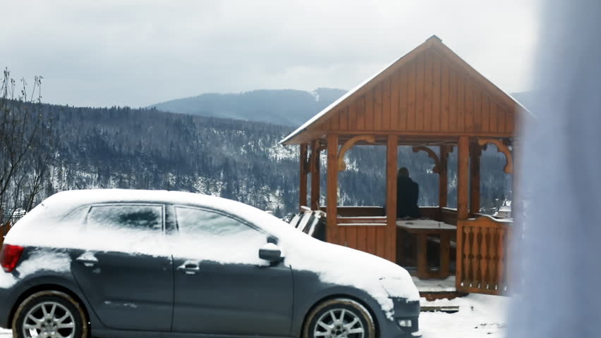 Guy observing the beautiful countryside from the wooden arbor in snowy weather on the large hills. Man traveling by car.