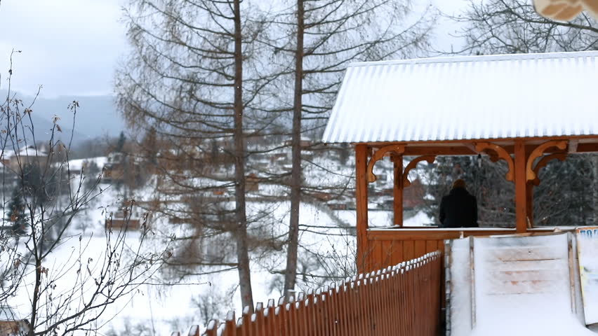 Back view of woman in pink coat on swings sitting looking around on snowy winter day. Amazing landscape in the background.