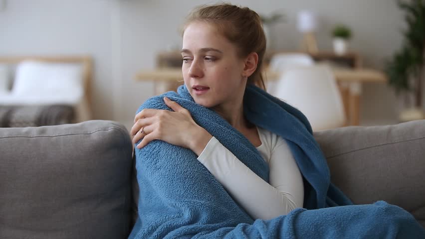 Sick  young woman feeling cold fever freezing no central heating problem at home covering with warm plaid blanket shivering sitting on couch got flu influenza virus grippe symptoms concept | Shutterstock HD Video #1025732642
