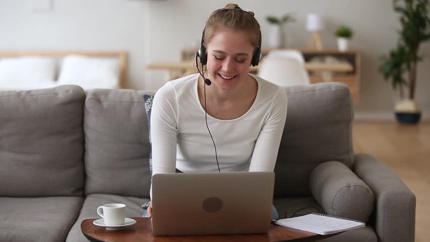 Happy young woman sales representative teacher in headset speaking to client making video conference call looking at laptop writing notes talking by webcam sell online work from home, telemarketing Royalty-Free Stock Footage #1025732654