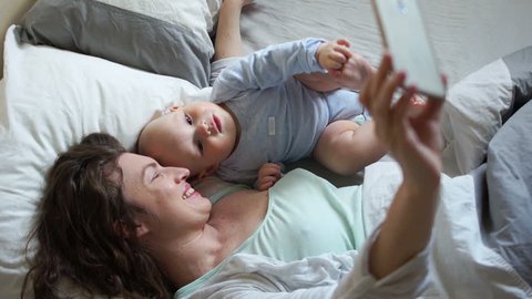 Toddler and his mom take a selfie lying in bed in the morning. Sunny spring morning, mother's day