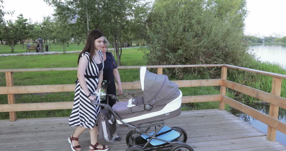 In the city park walk young mother and son on wooden bridge