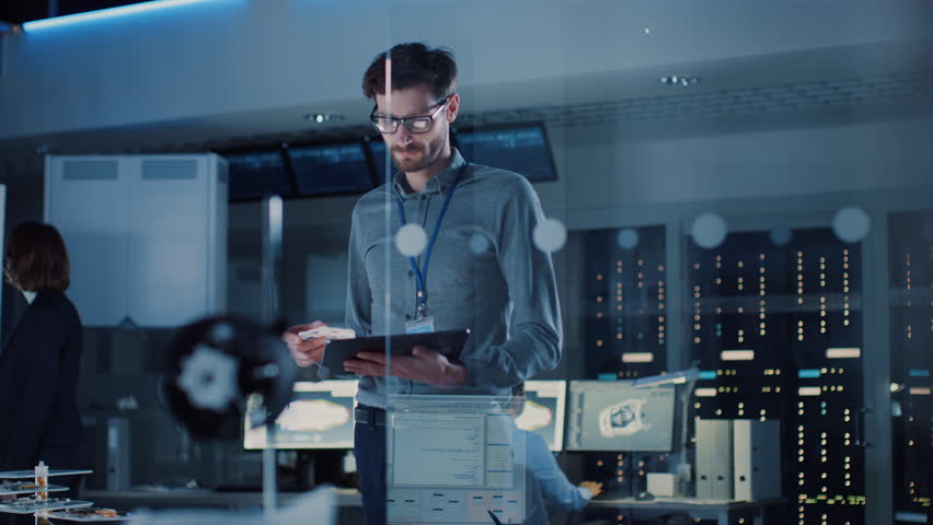In Technology Research Facility: Chief Engineer Stands in the Middle of the Lab and Uses Tablet Computer. Team of Industrial Engineers, Developers Work on Engine Design Use Digital Whiteboard Royalty-Free Stock Footage #1025738111