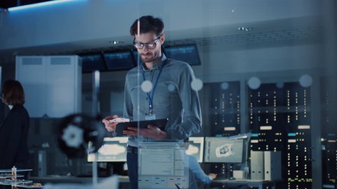 In Technology Research Facility: Chief Engineer Stands in the Middle of the Lab and Uses Tablet Computer. Team of Industrial Engineers, Developers Work on Engine Design Use Digital Whiteboard