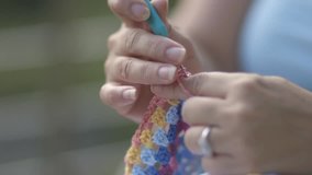 Close up of a woman crocheting a colorful blanket outdoor.