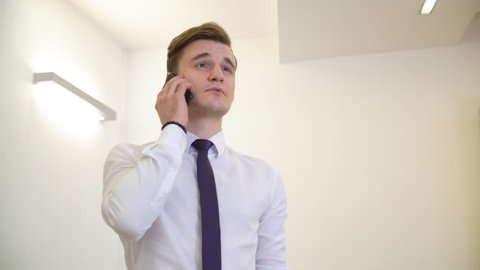 Young business man in white shirt and tie talking by mobile phone on white background. Handsome man entrepreneur calling smartphone in business office. Male portrate low angle