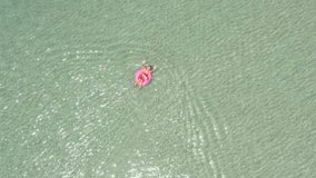 DRONE shot- happy woman waving hello enjoying beach holidays on tropical Island relaxing on inflatable flamingo floating on pristine clear sea. People vacations exoticism concept 