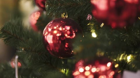 Closeup of several red plastic christmas balls hanging on christmas fir artificial tree. Gimbal tilt up shot of artificial christmas green tree with red christmas tree balls indoors.