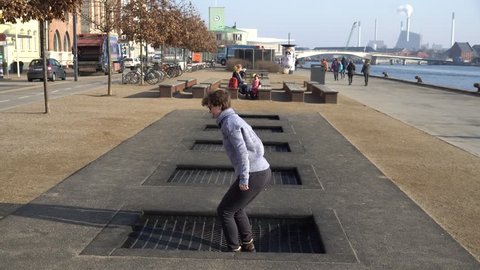 adult person rejoices like child. Playground trampoline in ground, children trampoline, springs throws people up fun and cool. Copenhagen River Embankment Denmark. Woman jumping on street trampoline.