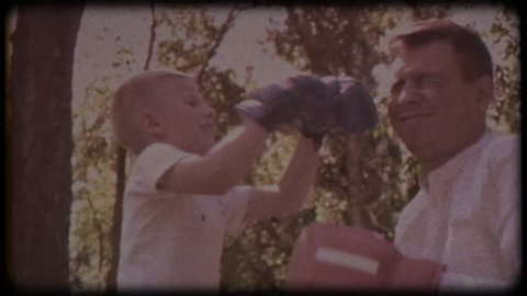 Family video archive. Retro camera 8 mm. Old film. Father and son in boxing gloves play boxing on the lawn near the house. happy childhood.